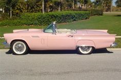 an old pink car is parked on the side of the road in front of some bushes