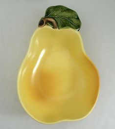 a yellow ceramic dish with a green leaf on the top and an eggplant decoration