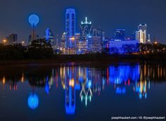 the city skyline is lit up at night with bright lights reflecting in the still water