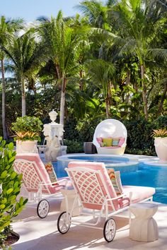 two lawn chairs sitting next to a swimming pool with palm trees in the back ground