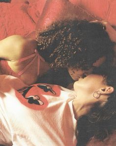 two women laying on top of a bed next to each other with their heads together