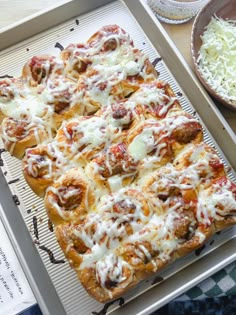 a pizza sitting on top of a pan covered in cheese and meat sauce next to a bowl of grated parmesan cheese