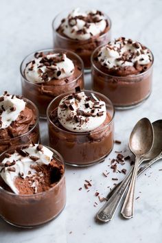 four desserts with chocolate and whipped cream in small glass dishes on a marble surface