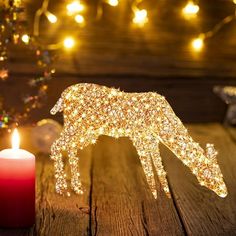 a lighted deer figurine next to a lit candle on a wooden table with christmas lights in the background