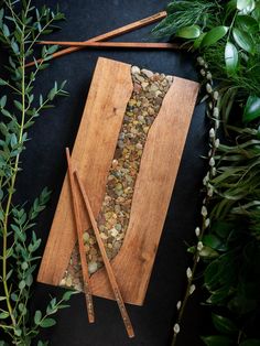 two chopsticks on a cutting board next to some herbs and rocks in the shape of a rectangle