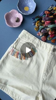 a pair of white shorts with colorful tassels on the side next to a bowl