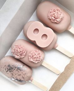 three pops with pink frosting and flowers on them sitting in a box next to each other