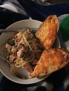 a white bowl filled with pasta and meat on top of a blue blanket next to a fork