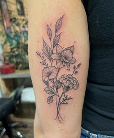 a black and white flower tattoo on the left upper arm, with leaves and flowers