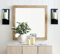 a vase with some candles sitting on top of a wooden cabinet next to a mirror