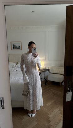 a woman in a white dress taking a selfie with her cell phone while standing next to a bed