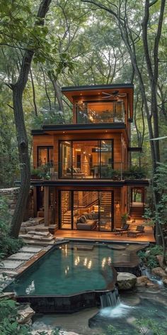 a house in the woods with a pool and waterfall running through it's front yard