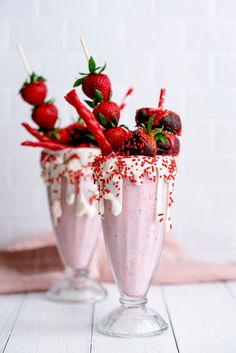 two glasses with strawberries and whipped cream in them on a white table next to a brick wall