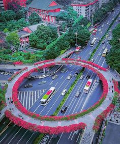 an aerial view of a city street with cars and buses on the road, surrounded by red flowers