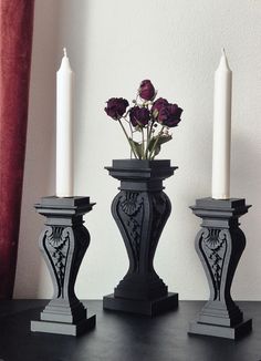 three candles are sitting next to each other on a table with flowers in the middle