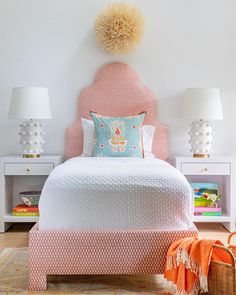 a bedroom with pink and white bedding, two nightstands and lamps on either side