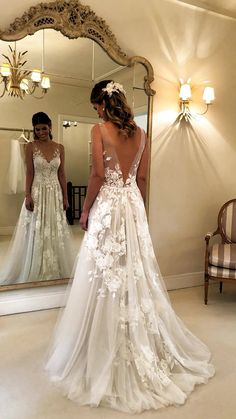 a woman in a wedding dress looking at herself in the mirror with her back to the camera