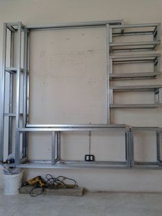 an empty room with metal shelves and tools on the floor next to a bucket full of wires