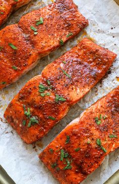 four cooked salmon fillets sitting on top of a piece of parchment paper with parsley