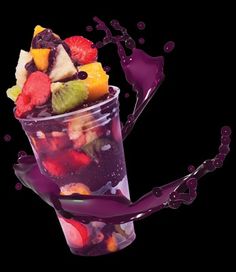 a cup filled with fruit and liquid on top of a black background