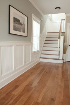 an empty room with stairs and pictures on the wall in front of the door, along with hardwood flooring