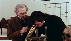 two men looking at an object in a room with skulls on the floor and tables