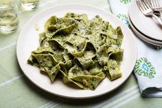 a white plate topped with green pasta next to silverware and glasses on a table