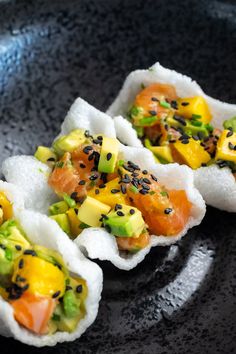 three pieces of sushi on a black plate with sesame seeds and avocado