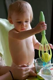 a baby holding a whisk in it's hand while being held by an adult