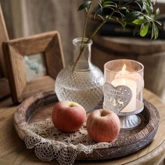 two apples on a tray next to a vase with a rose in it and a candle