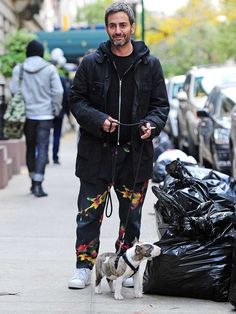 a man walking his dog down the street with trash bags on the sidewalk behind him