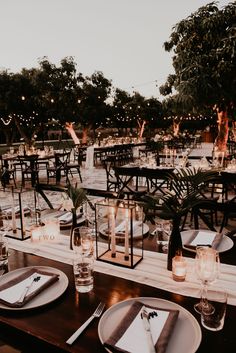 tables set up with candles and place settings for an outdoor wedding reception in the evening