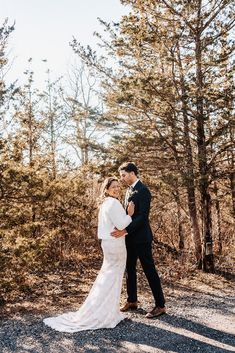 a bride and groom standing in the woods