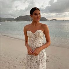 a woman standing on top of a sandy beach next to the ocean wearing a white dress