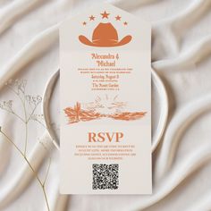 an orange and white wedding card with a cowboy hat on the front is sitting on a plate