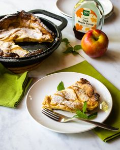 a piece of pie on a plate next to an apple and mint leafy garnish