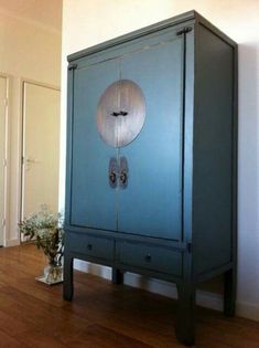 a blue cabinet sitting on top of a hard wood floor next to a vase with flowers