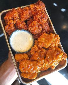 a person holding a tray full of food with sauce in it and chicken wings on the side