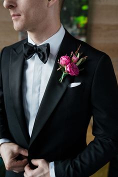 a man wearing a black tuxedo with a pink flower in his lapel