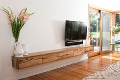 a flat screen tv sitting on top of a wooden shelf next to a vase with flowers