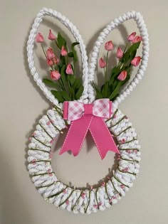 a white wreath with pink flowers and a pink bow hanging on the front of it