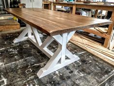 a large wooden table sitting on top of a floor next to a pile of wood