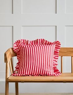 a red and white striped pillow sitting on top of a wooden bench next to a wall