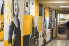 a man walking down a hallway next to a yellow and black wall with pictures on it