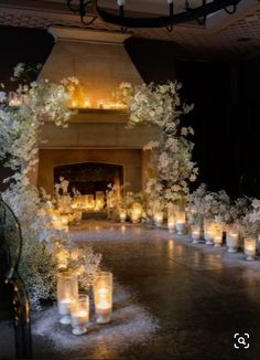 candles are lit on the floor in front of an open fire place with white flowers and greenery