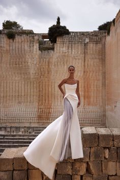 a woman standing on top of a stone wall wearing a white dress and matching heels