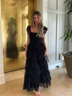 a woman standing in front of a door wearing a black tiered dress and flip flops