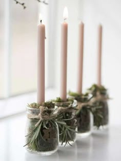 four candles are lined up in small glass jars with moss and pine cones on them