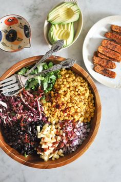 a wooden bowl filled with food next to other plates and utensils on a table