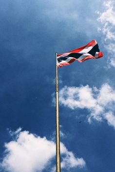 a flag flying high in the sky on a pole with a bird sitting below it